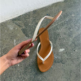 En hånd holder en brun og hvid flip-flop-sandal. Baggrunden er et råt, gråt betonunderlag ved en hvid væg.