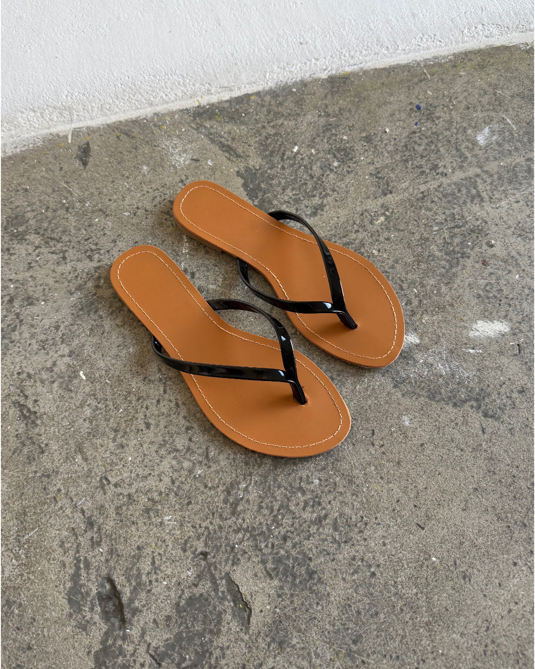 Et par brune flip-flops ligger stille på en grå, rå betonoverflade i et sparsomt belyst rum.