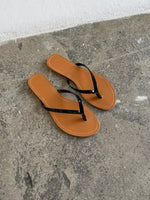Et par brune flip-flops ligger stille på en grå, rå betonoverflade i et sparsomt belyst rum.