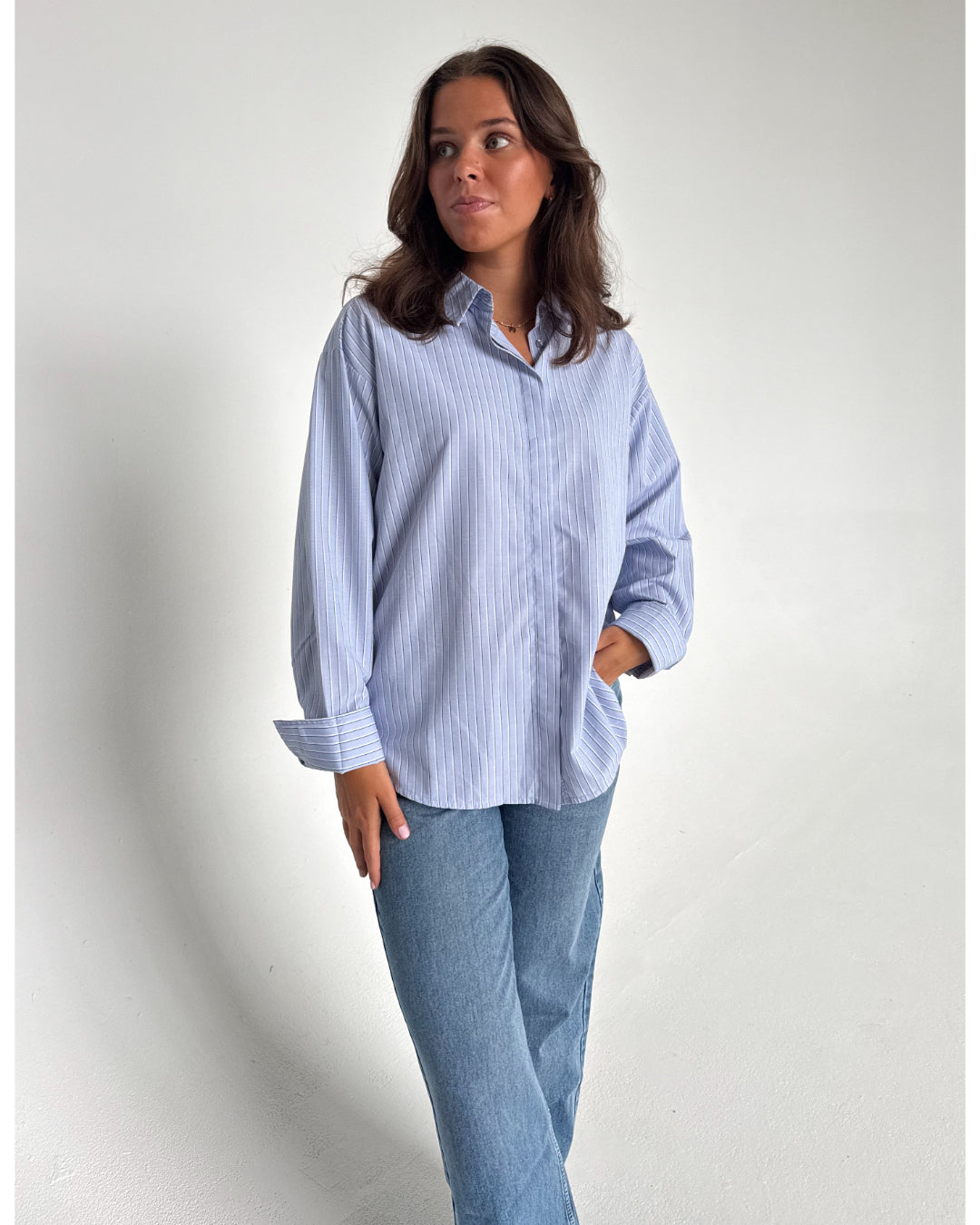 Modelfoto af pige der bærer en lyseblå stribet Caro skjorte, samt blå Nanna jeans. Alt fra BySofieSønderby