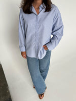 Modelfoto af pige der bærer en lyseblå stribet Caro skjorte, samt blå Nanna jeans. Alt fra BySofieSønderby