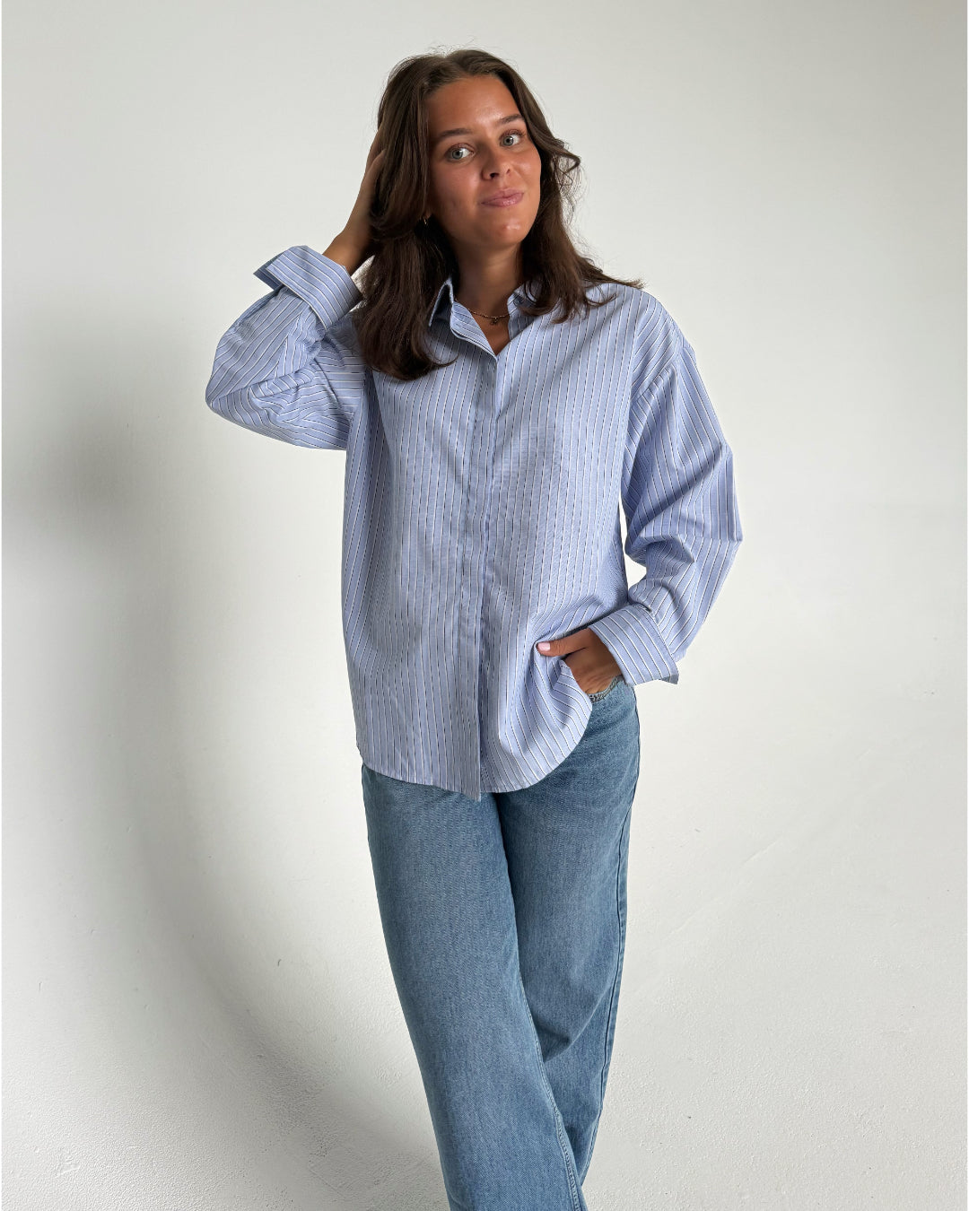 Modelfoto af pige der bærer en lyseblå stribet Caro skjorte, samt blå Nanna jeans. Alt fra BySofieSønderby
