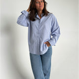 Modelfoto af pige der bærer en lyseblå stribet Caro skjorte, samt blå Nanna jeans. Alt fra BySofieSønderby