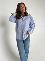 Modelfoto af pige der bærer en lyseblå stribet Caro skjorte, samt blå Nanna jeans. Alt fra BySofieSønderby