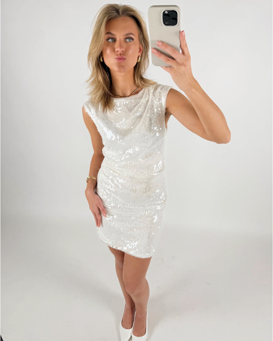 En person iført en glitrende hvid kjole tager en selfie. Personen laver en kysmund, står i et lyst rum, og bærer hvide sko.
