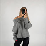 En person iført grå sweater tager et selfie med en smartphone. De står i et neutralt, lys baggrund.