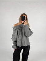 En person iført grå sweater tager et selfie med en smartphone. De står i et neutralt, lys baggrund.