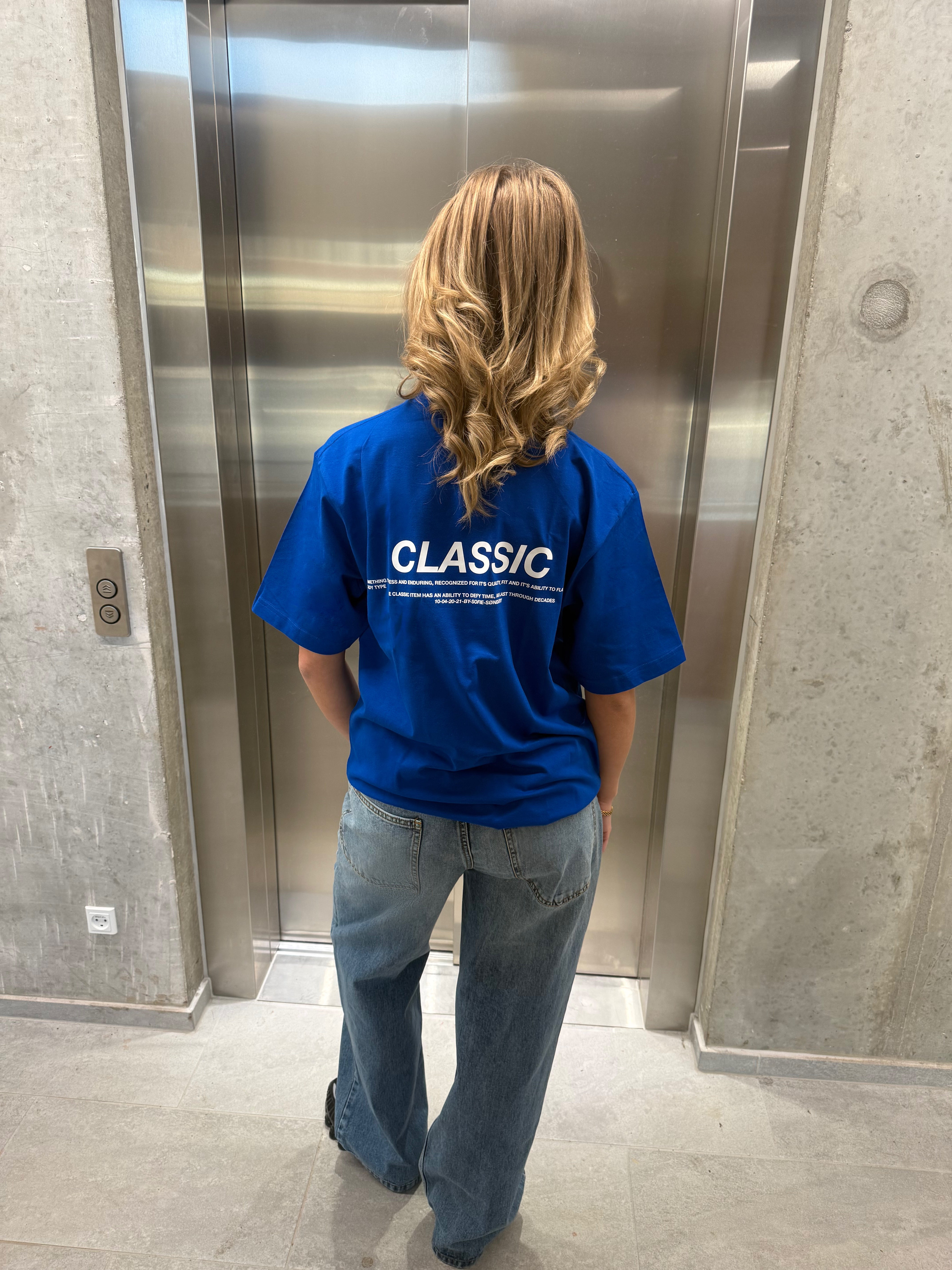 Stemningsbillede af pige der bærer en kongeblå t-shirt med hvidt classic tryk og blå NANNA jeans.  Fra BySofieSønderby