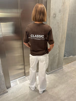 Stemningsbillede af pige der bærer en brun t-shirt med hvidt classic tryk og hvide NANNA jeans.  Fra BySofieSønderby