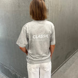 Stemningsbillede af pige der bærer en grå t-shirt med hvidt CLASSIC tryk og hvide NANNA jeans.  Fra BySofieSønderby