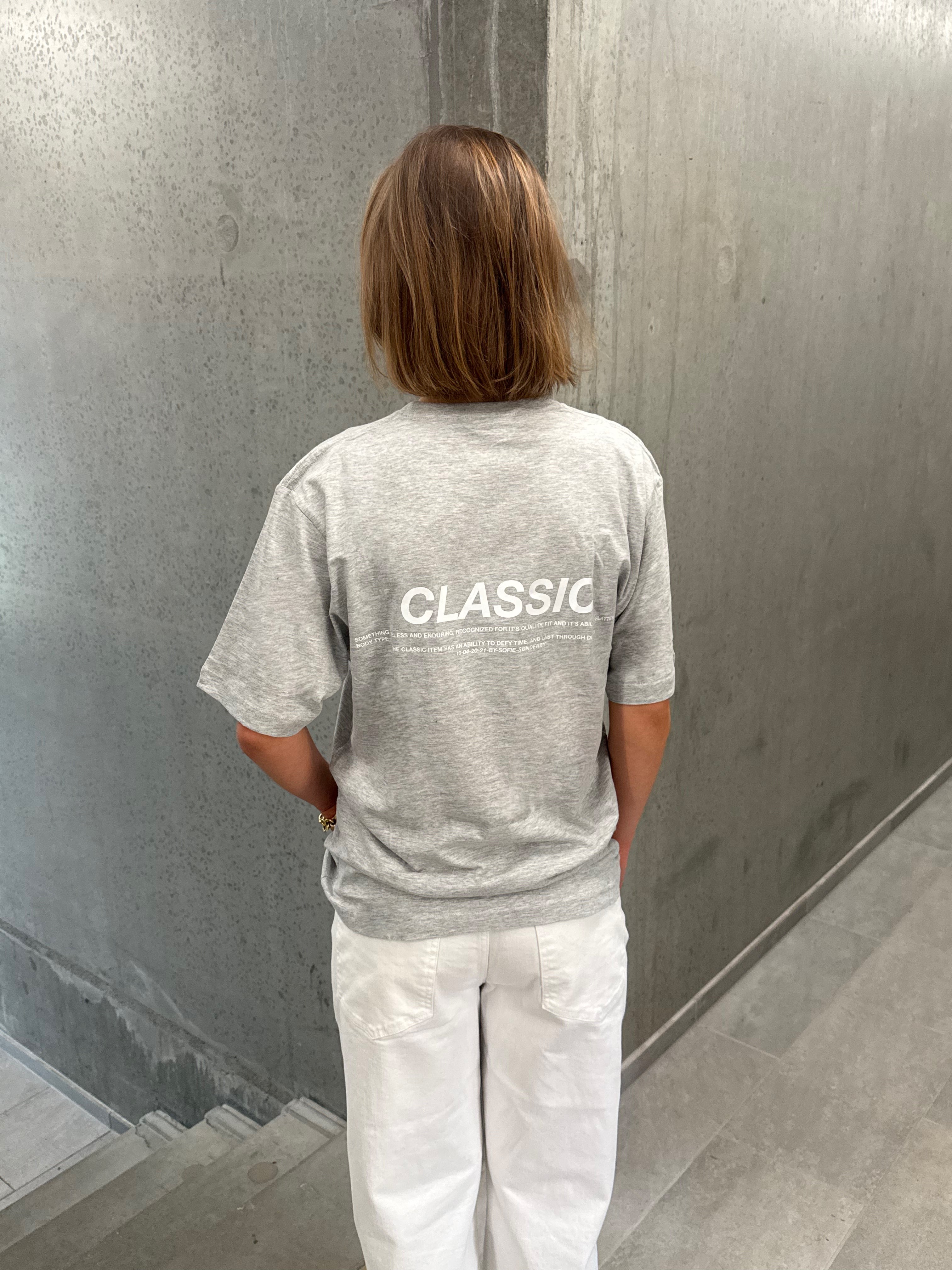 Stemningsbillede af pige der bærer en grå t-shirt med hvidt CLASSIC tryk og hvide NANNA jeans.  Fra BySofieSønderby