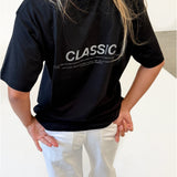 Modelfoto af pige i sort CLASSIC t-shirt med reflekstryk, samt hvide NANNA jeans. Alt er fra BySofieSønderby.