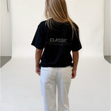 Modelfoto af pige i sort CLASSIC t-shirt med reflekstryk, samt hvide NANNA jeans. Alt er fra BySofieSønderby.