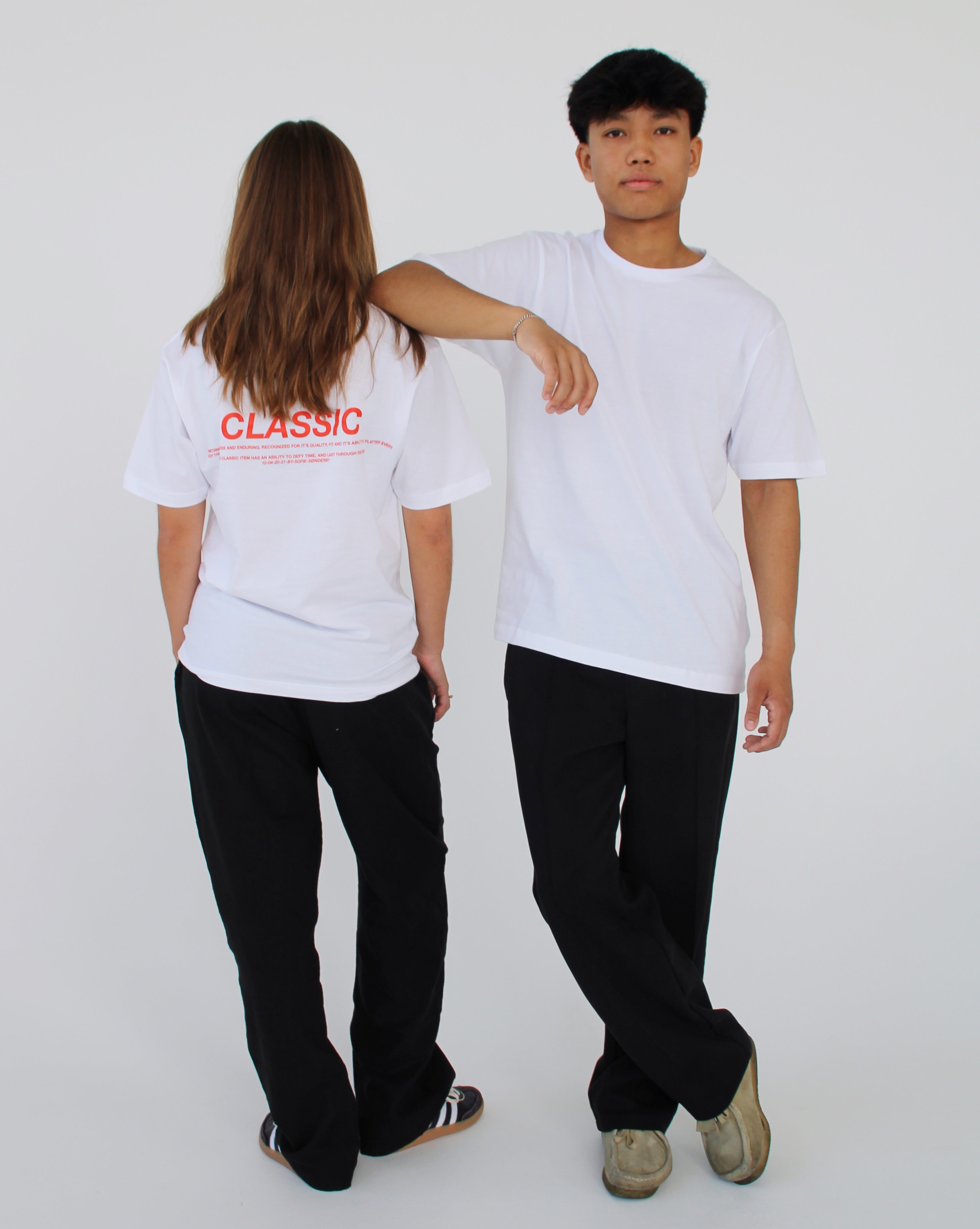 To personer iført hvide T-shirts og sorte bukser står sammen; den ene vender ryggen til med teksten "CLASSIC" på ryggen, den anden læner armen over den første i en neutral indstilling.