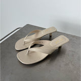Beige sandaler med hæl står på en grå metaloverflade. Venstre sandal har tekst "7C82 39", højre "CII". Baggrunden er enkel og lysegrå.