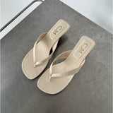Beige sandaler med krokodillemønster ligger på en grå overflade. Tekst på indersålen viser "CM Made in China".
