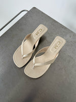 Beige sandaler med krokodillemønster ligger på en grå overflade. Tekst på indersålen viser "CM Made in China".