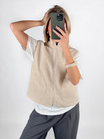 Modelfoto af pige i beige DAWN vest, hvid t-shirt og grå LISA bukser. Alt er fra BySofieSønderby.