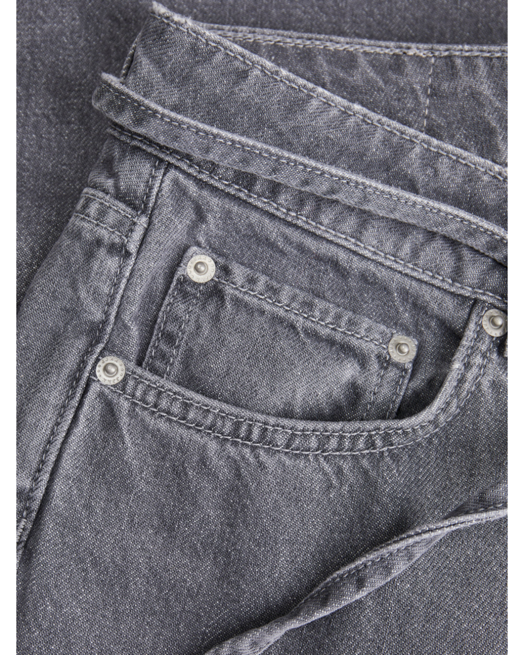 Grå jeans med synlige stikninger og metalnitter, der ligger fladt. Beliggende i en neutral baggrund uden tekst eller detaljer.