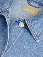Denimjakke med syning ses tæt på. En sølvknap med teksten "JACK&JONES" er synlig. Mærket "JJXX" i gul står ved kraven.