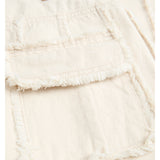 En beige denimjakke med frynset detalje på lommen. Tekst på en brun etiket viser "JJXX". Jakken ligger fladt i en lys kontekst.