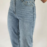 Et par lyseblå jeans bæres, med fokus på hofte- og lommedetaljer. Jeansene har en høj talje, lynlåsgylp og sidder i et neutralt studio-tagningsmiljø med hvid baggrund.