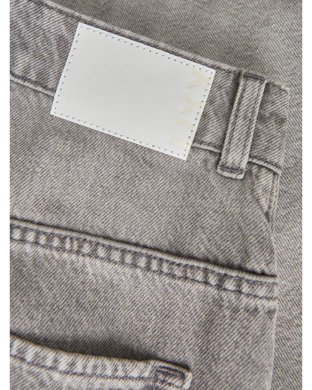 Grå denimstof viser et baglommeområde med bæltestropper og en hvid mærkat syet på. Tekst på mærkaten siger "LIV".