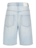 Lyseblå denimshorts vises fra bagsiden. De har to baglommer og et hvidt mærke på linningen. Korssting dekorerer lommerne. Baggrunden er ensfarvet hvid.