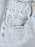 Lyseblå denimstof med synlige lommer og sølvfarvede nitter. Stitching er i kontrasterende gult tråd, og en bæltestrop er synlig. Stoffet har en let struktureret overflade.
