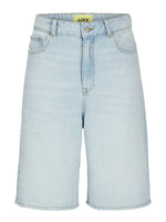 Lyseblå denimshorts med klassisk femlommers design. De står oprejst og viser et guldfarvet mærke indeni, med teksten "JJXX". Baggrunden er hvid og neutral.