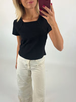 Kvinde iført sort bluse tager selfie med en rød telefon. Hun står i lyse, vide bukser i et lyst rum. Hun har pink neglelak og gyldent blondt hår.