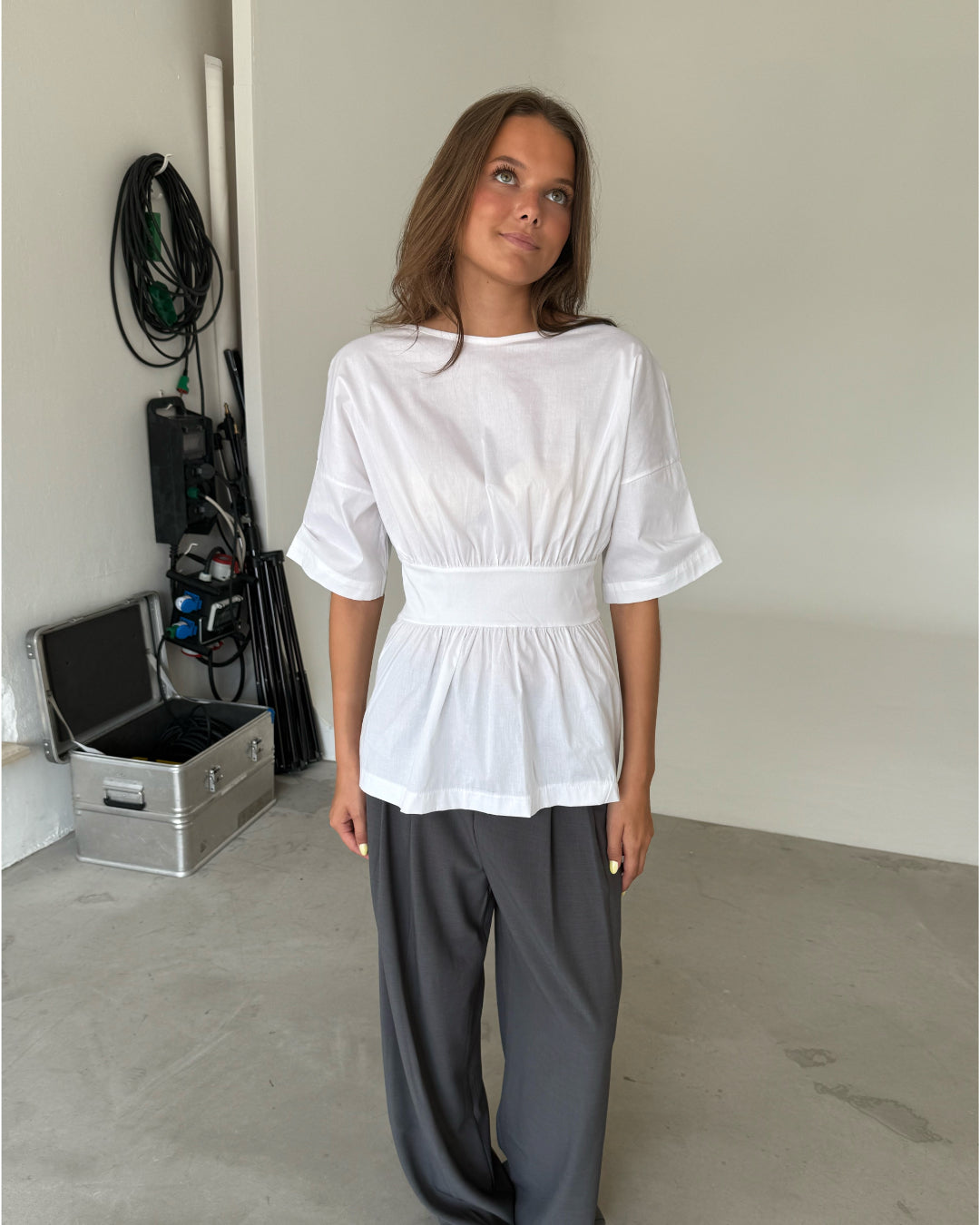 Modelfoto af pige som bærer en hvid ESTRELLA bluse med bindebånd på ryggen, samt grå kontorbukser. Alt er fra BySofieSønderby