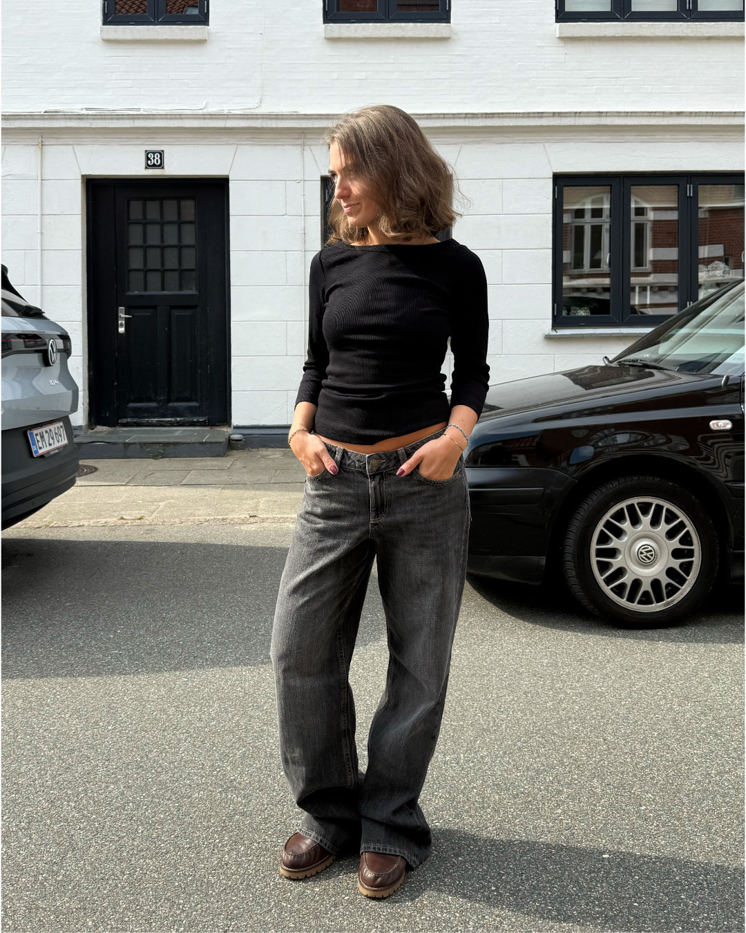 Modelfoto af pige i en sort Fifi boatneck bluse og grå Nanna jeans. Alt er fra BySofieSønderby