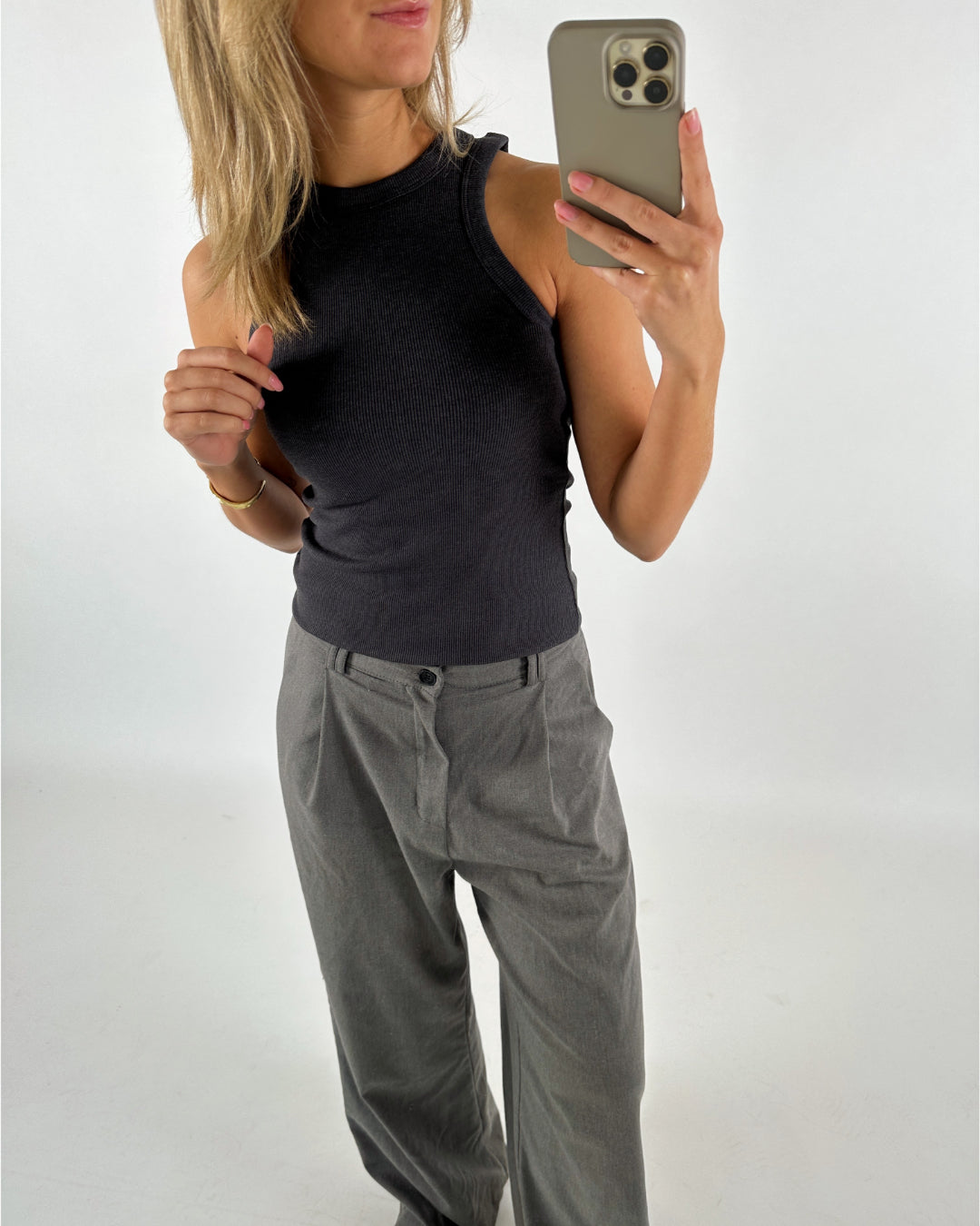 En person iført sort tanktop og grå bukser tager et spejlbillede med en smartphone i et lyst rum.