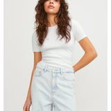 En person står afslappet iført en hvid T-shirt og lyse denim jeans. Konteksten er en simpel, lys baggrund. Ingen tekst er til stede.