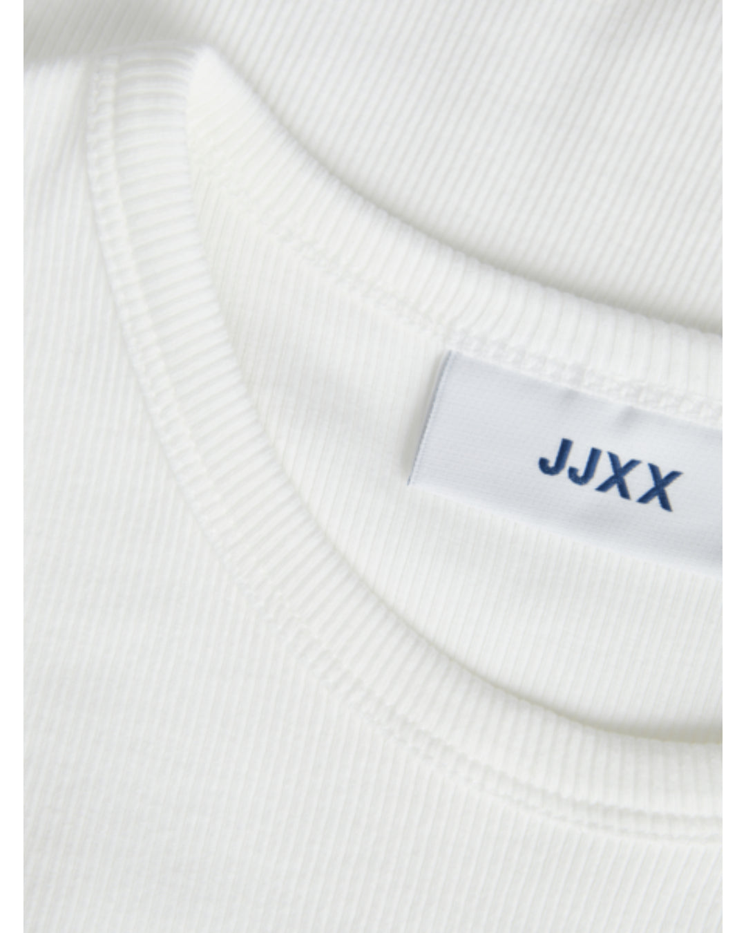 En hvid trøje med mærkatet "JJXX" syet ind i nakken, ligger fladt på en lys overflade.