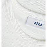 En hvid trøje med mærkatet "JJXX" syet ind i nakken, ligger fladt på en lys overflade.