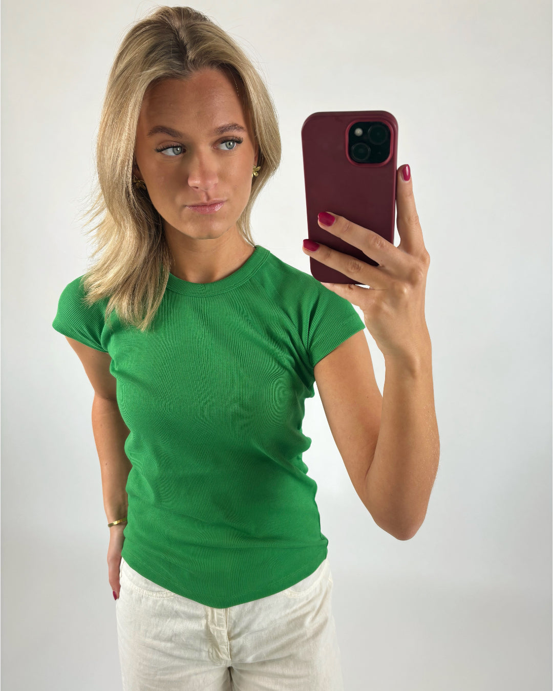 En person iført en grøn bluse tager en selfie med en smartphone i en rød etui. Baggrunden er ensfarvet hvid.