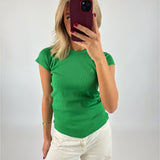 En person iført en grøn t-shirt tager en selfie med en smartphone i rød etui, står mod en neutral væg.