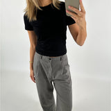 Person tager et spejlbillede iført sort T-shirt, grå bukser og røde sko i et minimalistisk rum. Personen holder en smartphone med et lysegråt cover.