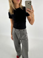 Person tager et spejlbillede iført sort T-shirt, grå bukser og røde sko i et minimalistisk rum. Personen holder en smartphone med et lysegråt cover.