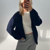 Person tager et spejlbillede med en smartphone, iført en mørk sweater og lyse bukser, i et minimalistisk, lyst rum uden tekst.