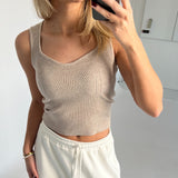 En person tager et spejlbillede iført en beige, ribbet tanktop og hvide joggingbukser. De holder en smartphone og står i et lyst rum uden tekst i baggrunden.