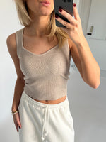 En person tager et spejlbillede iført en beige, ribbet tanktop og hvide joggingbukser. De holder en smartphone og står i et lyst rum uden tekst i baggrunden.