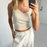 En person tager et spejlbillede iført en hvid top og joggebukser i et minimalistisk, lyst rum med en smartphone.