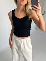En person iført sort top og hvide joggingbukser tager et spejlbillede i et minimalistisk rum. Personen holder en telefon, og der er ingen tekst i billedet.