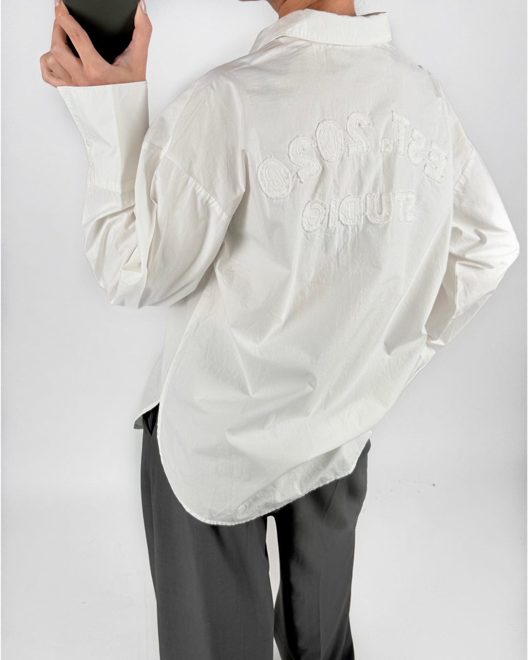 Modelfoto af pige i hvid HENNA skjorte med skrift-detaljer på ryggen, samt grå LISA bukser. Alt er fra BySofieSønderby.