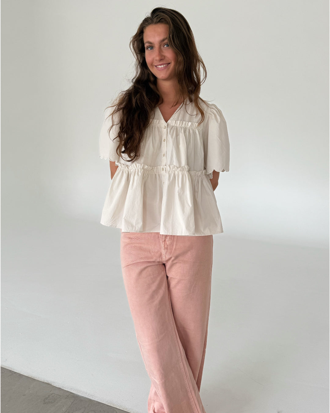 Modelfoto af pige som bærer creme-farvet HOPE top med v-hals og lyserøde jeans. Alt er fra BySofieSønderby