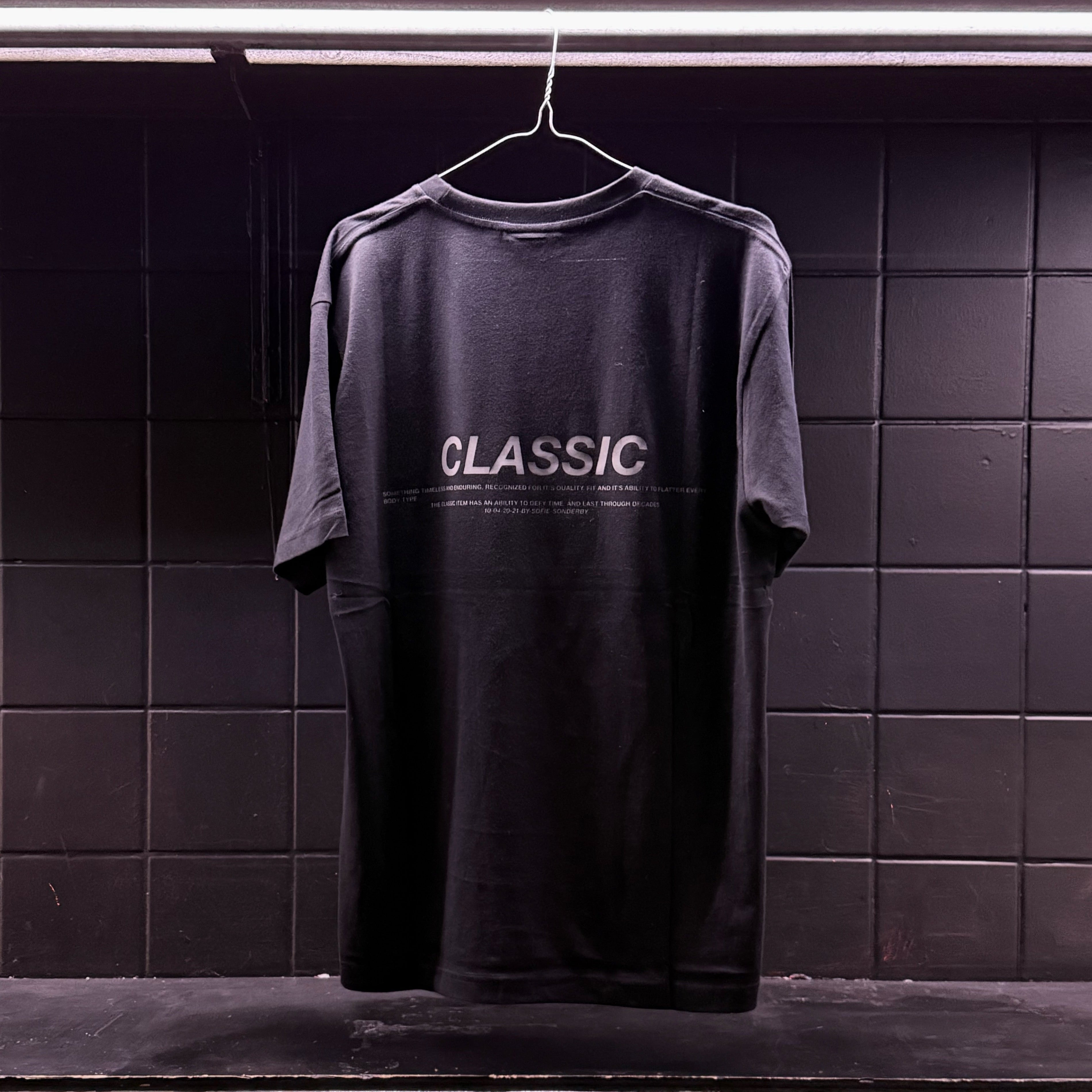 Stemningsbillede af sort t-shirt, med CLASSIC tryk, hængende på bøjle. Fra BySofieSønderby