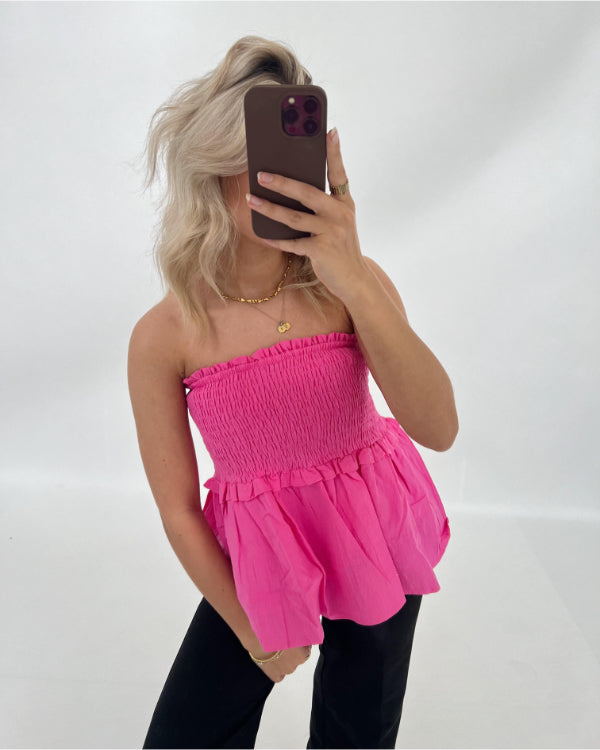 En person iført en lyserød stropløs top tager et selfie med en mobiltelefon. Personen står foran en lys baggrund.